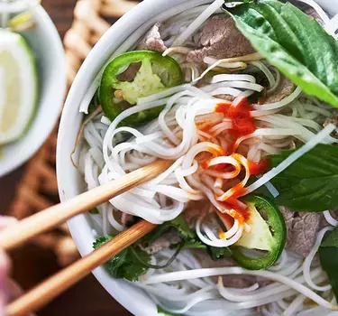 A bowl of Pho garneshed with jalapeno slices, basil, cilantro and lime.