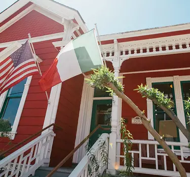 An immaculate, red and white Victorian home with the American and Italian flags flying in Little Italy.