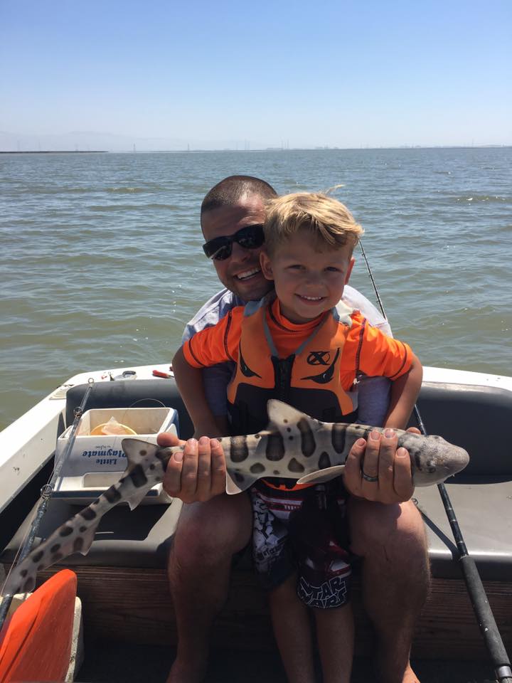 Man & boy sitting in a boat holding a small spotted shark