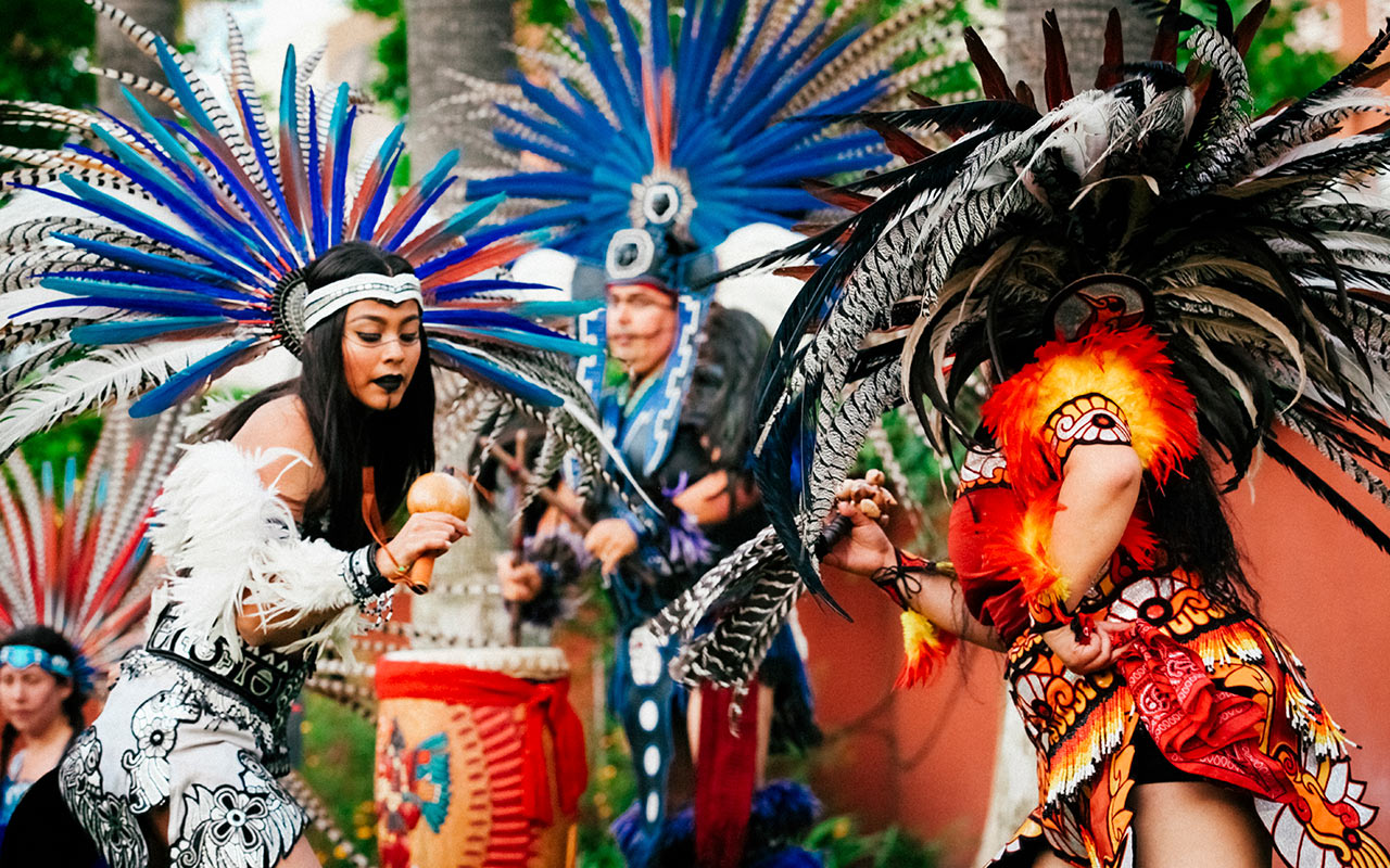 Aztec dancers performing around palm trees in the garden at the Mexican Heritage Plaza