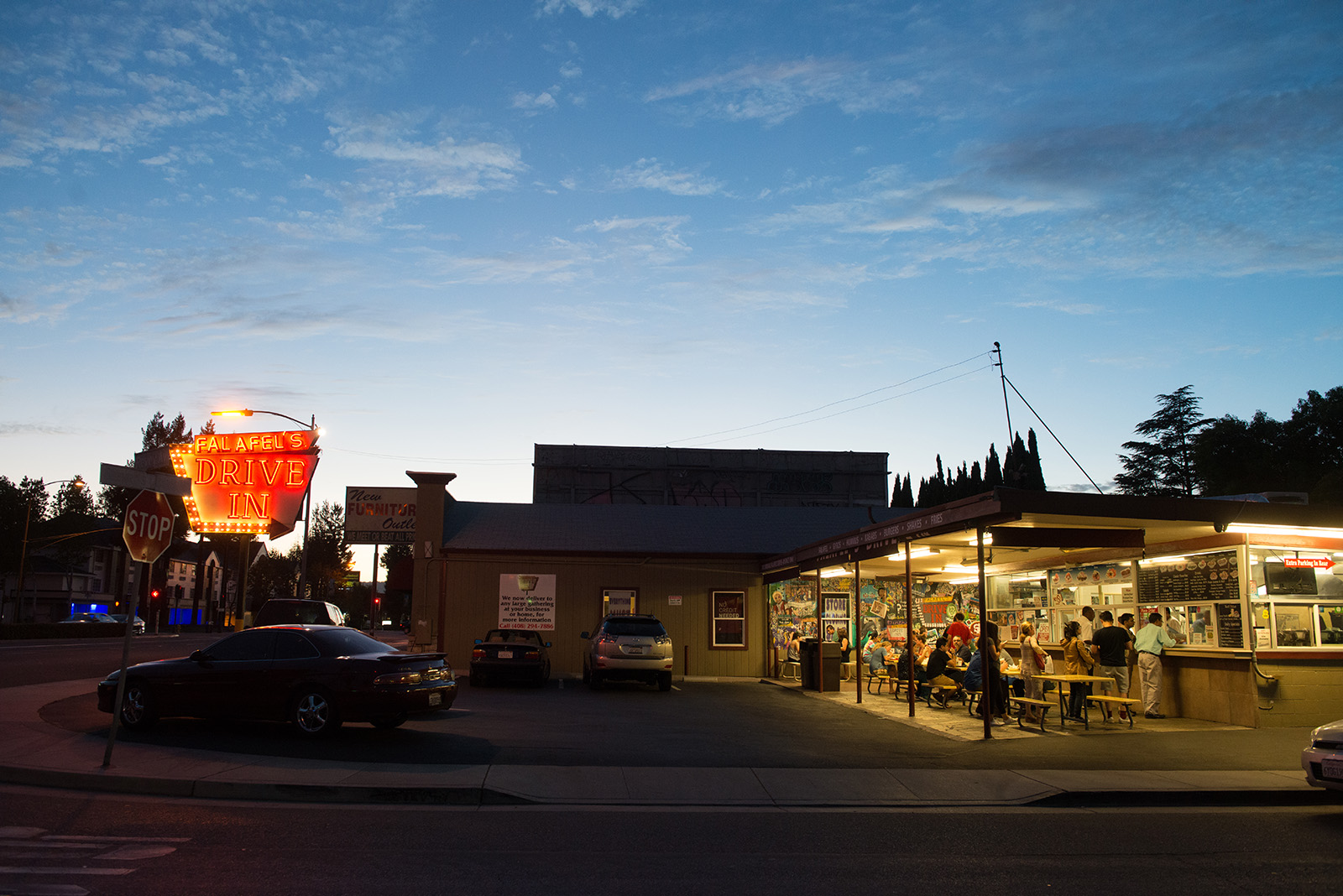 Falafel Drive-In neon sign lit up and people dining outside 