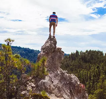 A hiker standing on top of a mountain peak in Big Basin Redwoods State Park overlooking the gorgeous redwood draped Big Basin Redwoods State Park