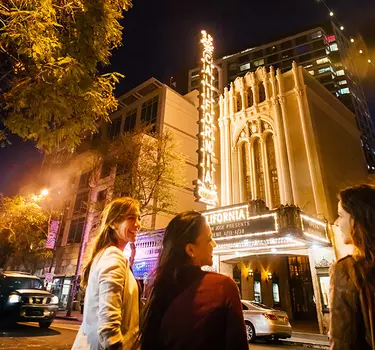 A group of ladies walking down First Street toward the California Theatre with it's historic marquee lit up