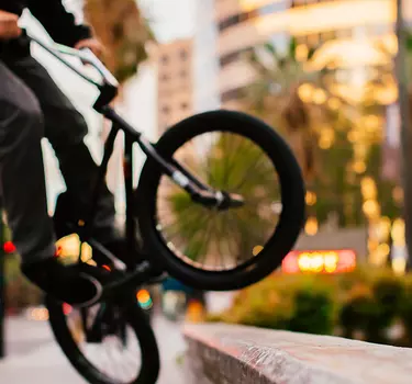 A guy on a bmx bike doing a trick on a cement block with buildings and palm trees in the background