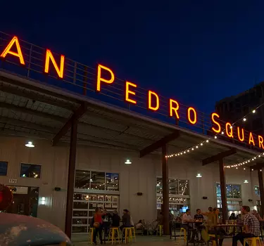 People mingling and dining on the front patio under the lit San Pedro Square Market sign