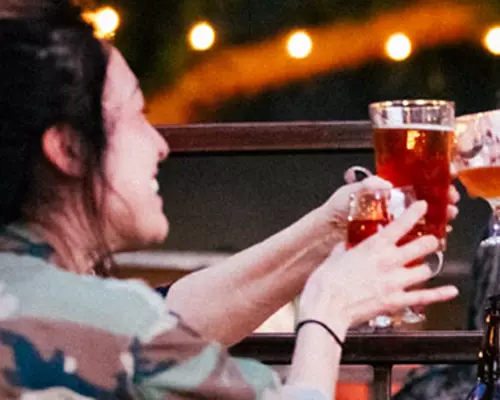 A group enjoying drinks and laughing on the San Pedro Square Market patio with lights in the trees