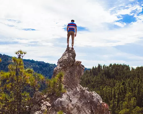 A hiker standing on top of a mountain peak overlooking the gorgeous redwood draped Big Basin Redwoods State Park